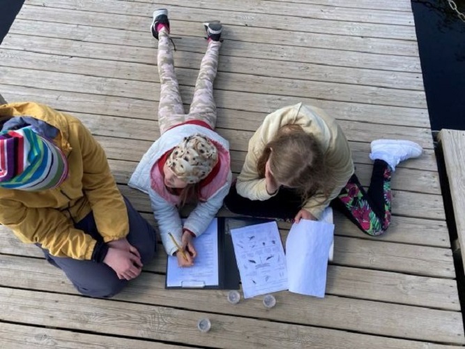 kolm last paadisillal, laste ees on topsluubid ja töölehed