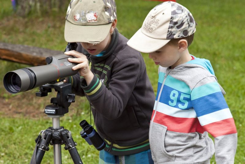 Kaks poissi, mõlemad nokamütsid peas, vaatlevad vaatlustoruga