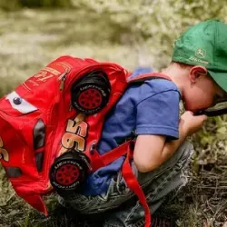 Rohelise nokamütsi ja punase seljakotiga poiss uurib luubiga loodust